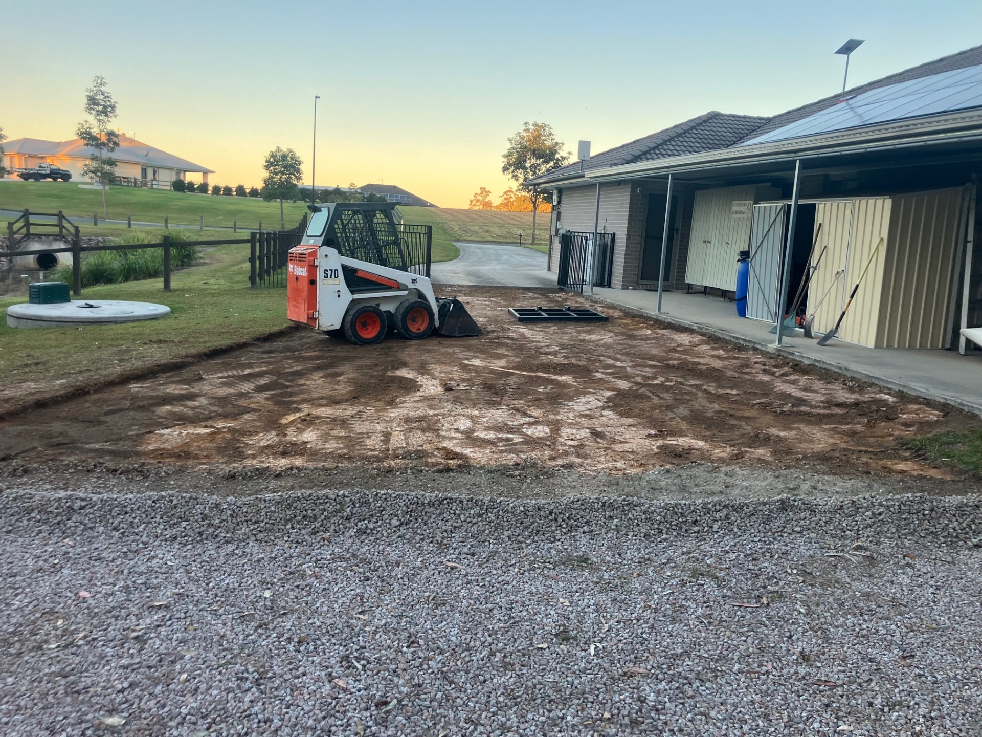 Bobcat S70 skid steer preparing a level pad beside a residential home at sunset