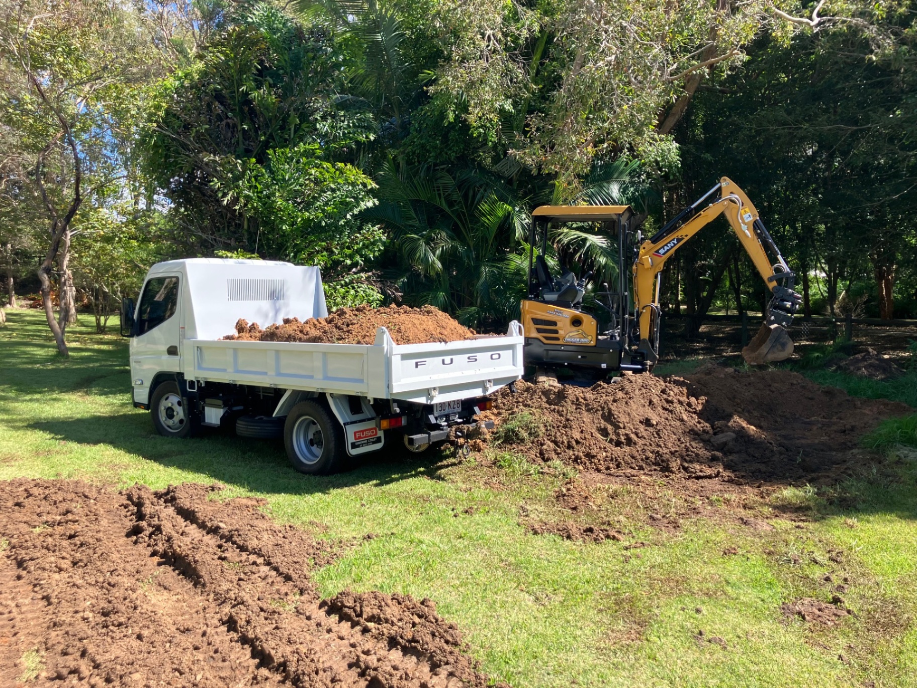 Digger Bro mini excavator loading soil into a Fuso tipper truck on a rural block