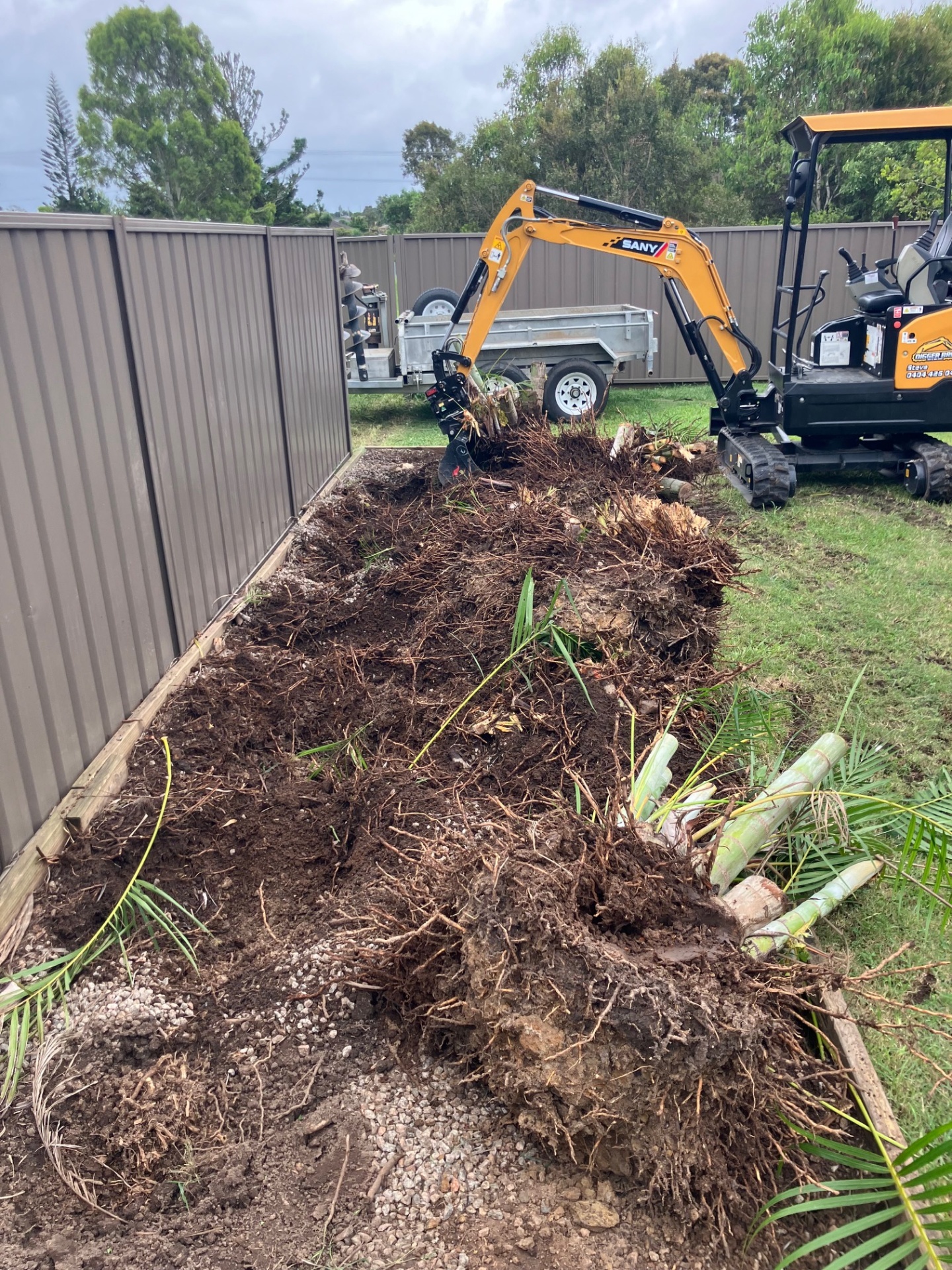 Digger Bro excavator clearing vegetation near a boundary fence